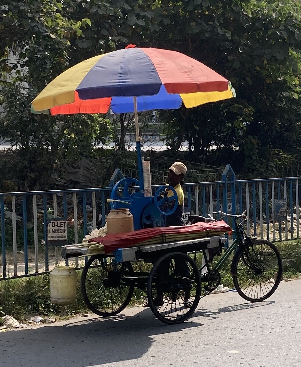 Vendor beside a bicycle-mounted machine topped by a multicolored umbrella