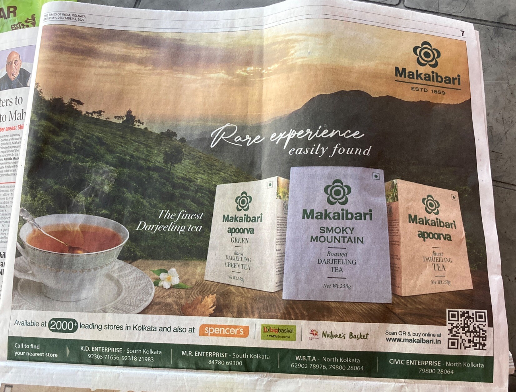 Cup of tea and boxes of Makaibari green, roasted, and (apparently) black tea, all seen against a vista of hilly tea gardens