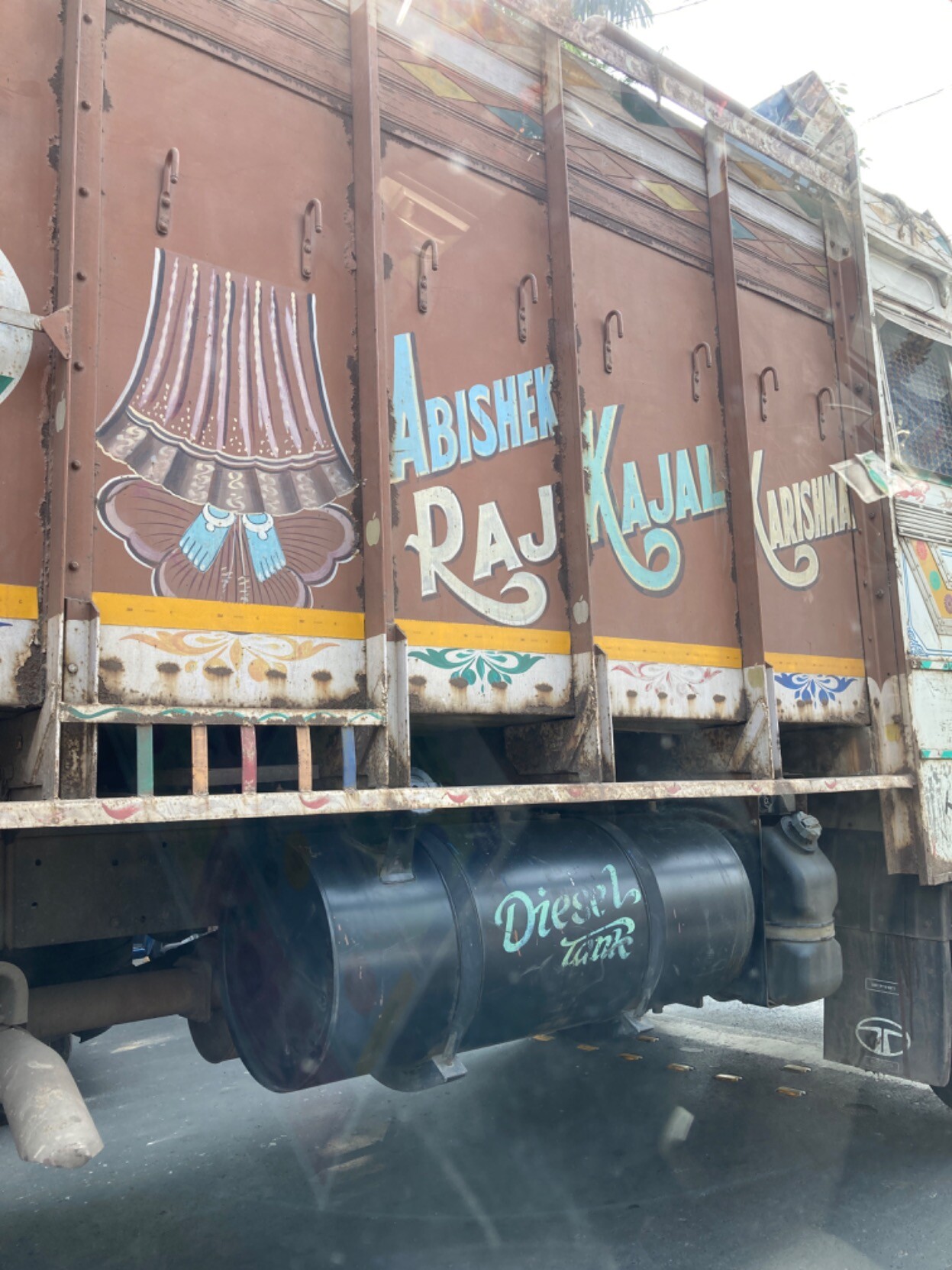 Side of a brown truck with an outboard fuel tank; in curvy blue and white lettering, “Raj Kashal Karishna”, plus a painting of a skirted, blue-footed deity from the waist down