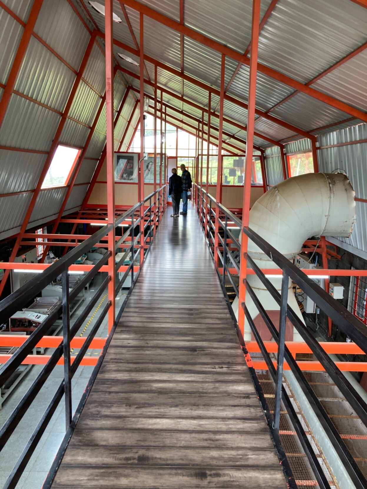Looking along a sort of catwalk under a glass roof above a factory floor