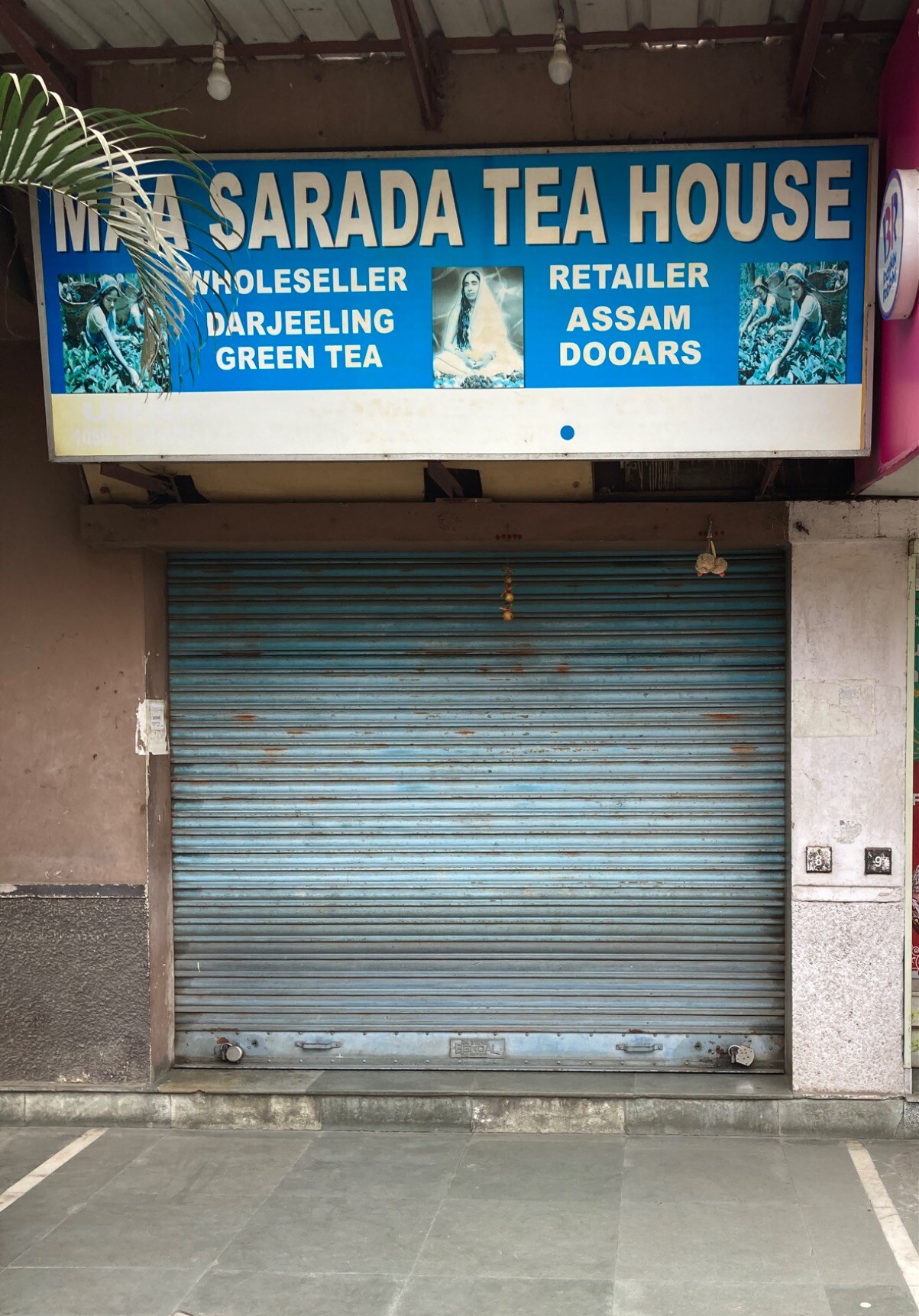 Locked up storefront with sign: MAA SARADA TEA HOUSE
WHOLESALER RETAILER
DARJEELING ASSAM
GREEN TEA DOOARS
