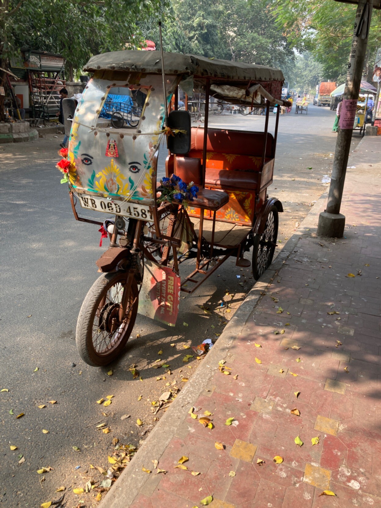Seen from the front, a bicycle rickshaw parked at the edge of a road with a windshield decorated with big eyes, scrollwork, and religious symbols?