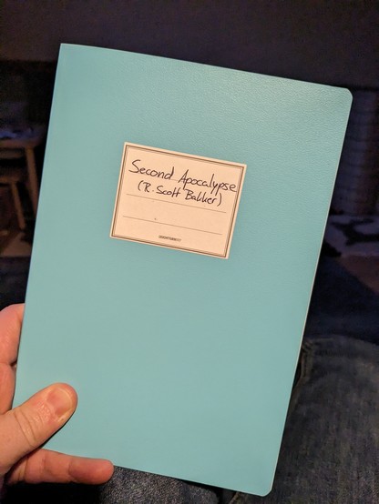 Foto des Covers eines hellblauen Notizbuchs mit der Beschriftung: "Second Apocalypse (R. Scott Bakker)