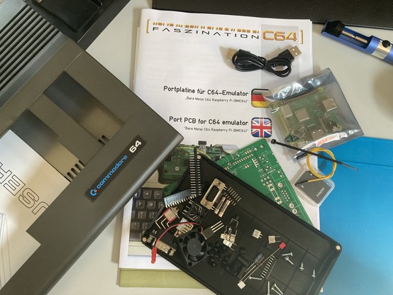 Eine Sammlung von elektronischen Bauteilen und Unterlagen auf einem Schreibtisch, die mit einem Commodore 64-Elektronikprojekt zusammenhängen, darunter eine Tastatur, Leiterplatten und Werkzeuge.