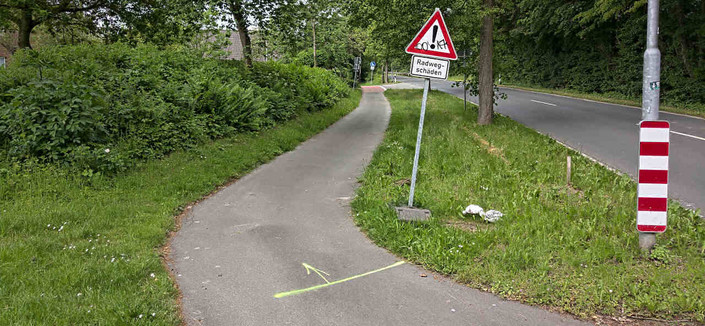 Ein Gehweg, der entgegen der eigentlichen Richtung für den Radverkehr freigegeben ist und der zusätzlich mit "Radwegschäden" beschildert ist.