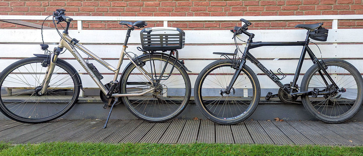 Links ein Bergamont Trekking-Damenrad mit Vorderradfederung und einem Fahrradkorb auf dem Gepäckträger. Rechts im Bild ein sog. Sports-Urban-Bike von Scott.