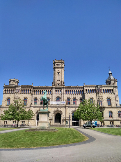 Photo of the main building of Leibnitz University of Hannover (in think).

Looks like a castle.

Also: Horse monument, green tree, blue sky.