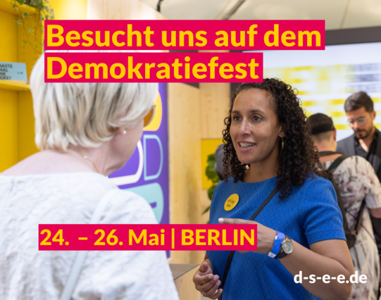 Foto mit Menschen, die sich am DSEE-Stand unterhalten. Text: Besucht uns auf dem Demokratiefest. 24. – 26. Mai | Berlin d-s-e-e.de