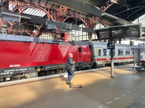 A red locomotive is pulling a white carriage with a red stripe into a train shed. (Presumably there are more carriages.)