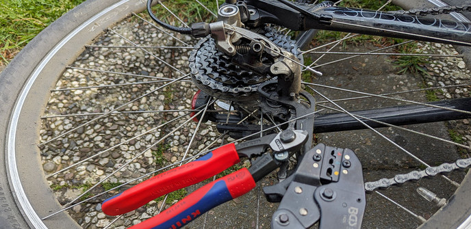 Das hintere Schaltwerke eines auf der Seite liegenden Fahrrads mit zwei Zangen, welche auf den Speichen drapiert sind.
