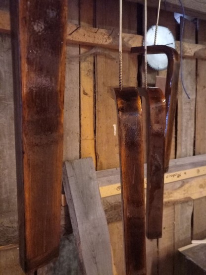 Four stool legs, stained dark with a worn effect and coated in glossy varnish that is still drying. They're hanging from the sealing of a wooden shack by some big screws.