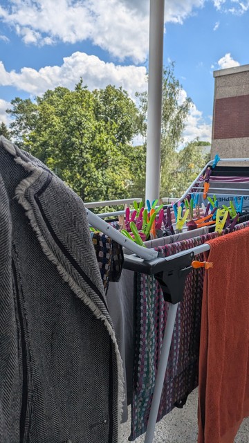 Wäscheständer mit verschiedenen Kleidungsstücken und vielen bunten Klammern auf Balkon