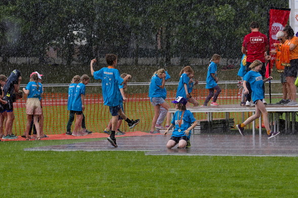Regenguß und viele Kinder mit blauen T-Shirts auf dem Weg zur Bühne.
Ein Kind tanzt im Regen.