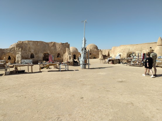 Mischung aus Star wars Rundkuppelhäuser und Flachdachhäuser wie man sie von Tatooine kennt, davor einige kleine Verkaufsstände und ein Sendemast, ebenfalls Teil der ehemaligen Filmkulisse