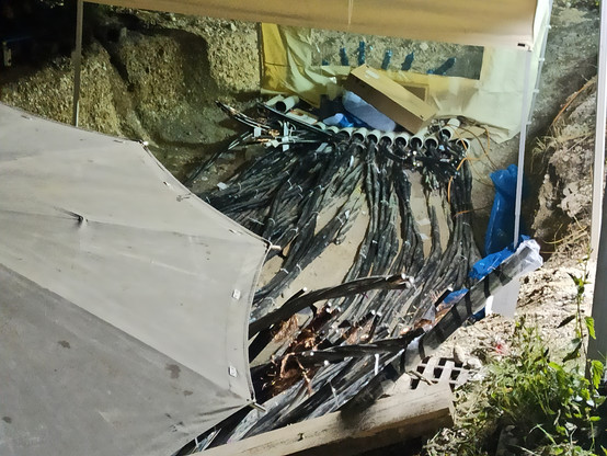 Eine Grube mit vielen schwarz ummanteltelten Stromkabeln, teilweise hängen Kabelenden herum. Im Vordergrund ein großer Regenschirm, der einen Teil der Grube verdeckt. Aufgenommen nach einem Brandanschlag in München 2021 als komplettes Stadtviertel mehrere Tage ohne Strom war und über 50 Mittelspannung-Kabel repariert werden mußten.