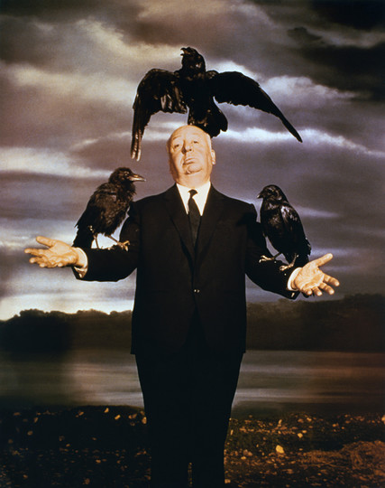 Alfred Hitchcock mit 3 schwarzen Vögeln auf den Armen und dem Kopf.