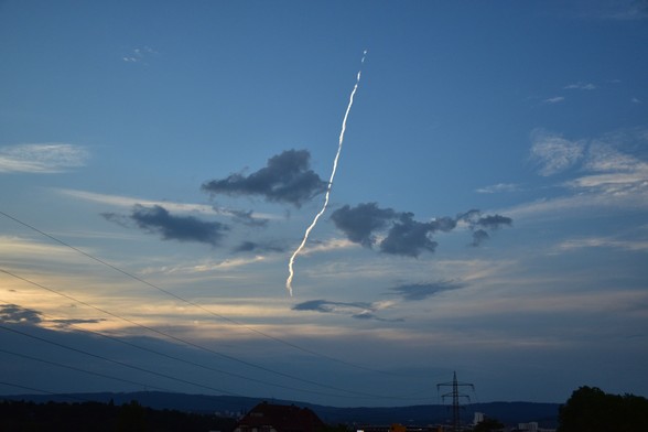 Vordergrund blauer Himmel. Im Hintergrund stecken Wolken am Taunuskamm fest. In Bildmitte ein strahlend weiß leuchtender Kondensstreifen.