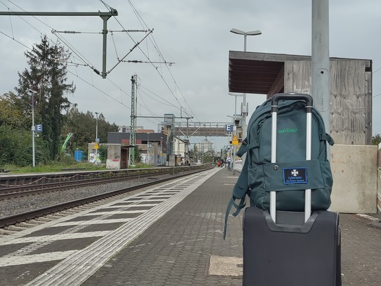 Gepäck an einem Bahnsteig. Im Hintergrund eine große provisorische Holzbrücke über die Gleise. Der Bahnhof scheint im Umbau.