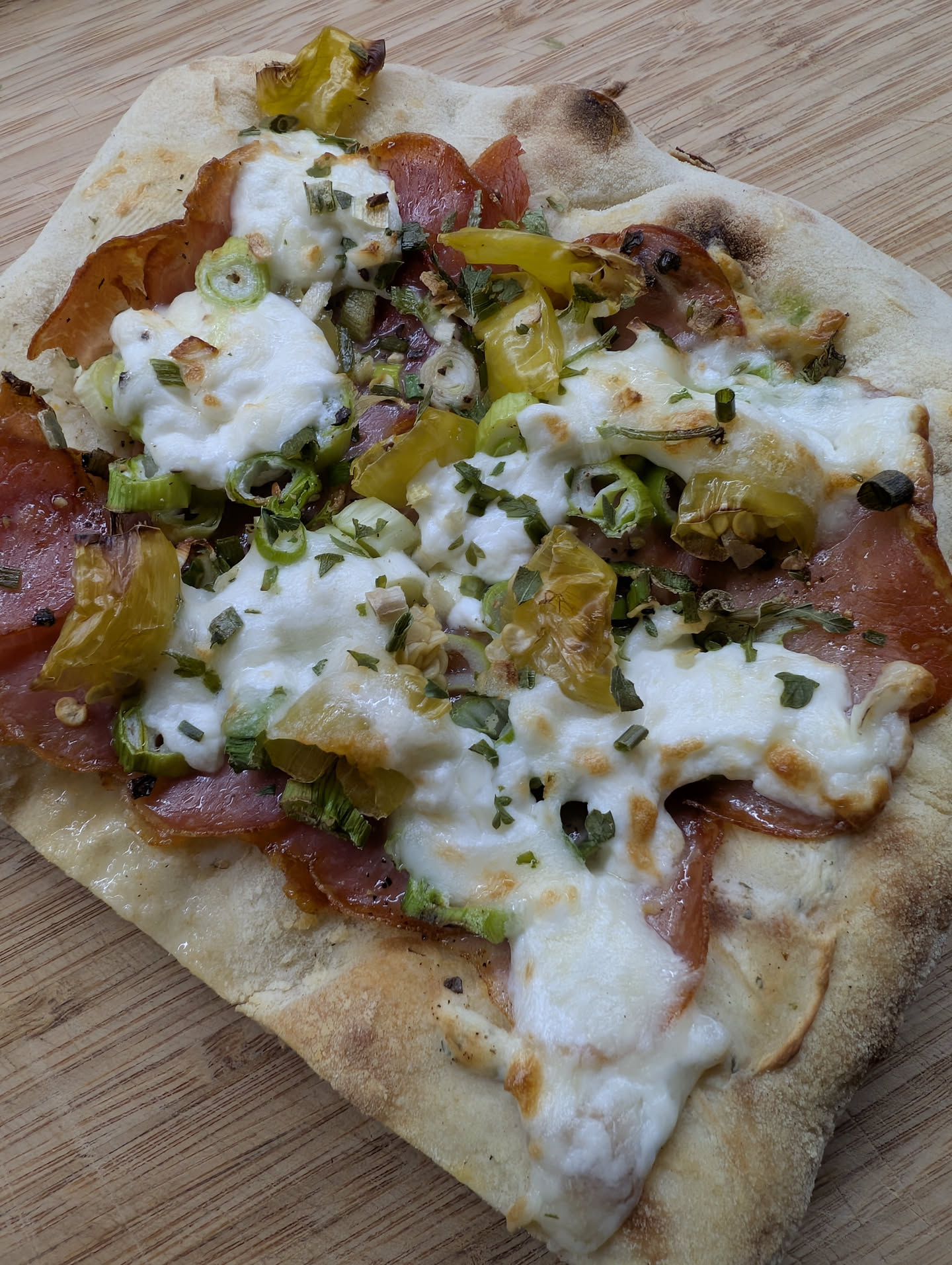 Üüberbackene Pinza mit Schinken, Burrata, Zwiebeln und Peperoni auf einem Holzbrett.