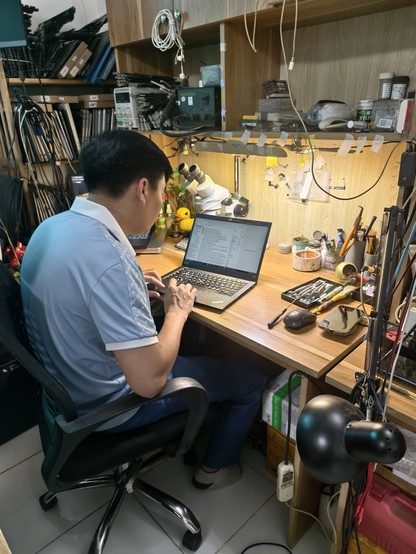 Computer repair in Hanoi, a worker sits with a laptop in front of His desky many tools left right and centre. Nicely lot. Mess and no mess at the same time 