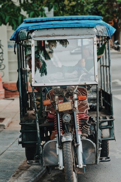 An old yet flash mini delivery truck 🚚 is parked on the corner of a street, the driver napping on the front seat 