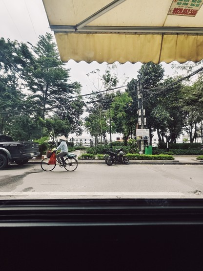 Snapshot looking out the window towards the street, cyclist driving along, the West Lake of Hanoi in the background. Listening to Jazz music 