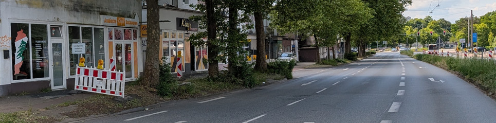 Ein zweispurige Straße mit einer zusätzlichen Spur für Linksabbieger. Der Blick geht entgegen der Fahrtrichtung und man sieht einen abgesperrten Radweg, auf welchem auch in Gegenrichtung zum Absteigen aufgefordert wird.