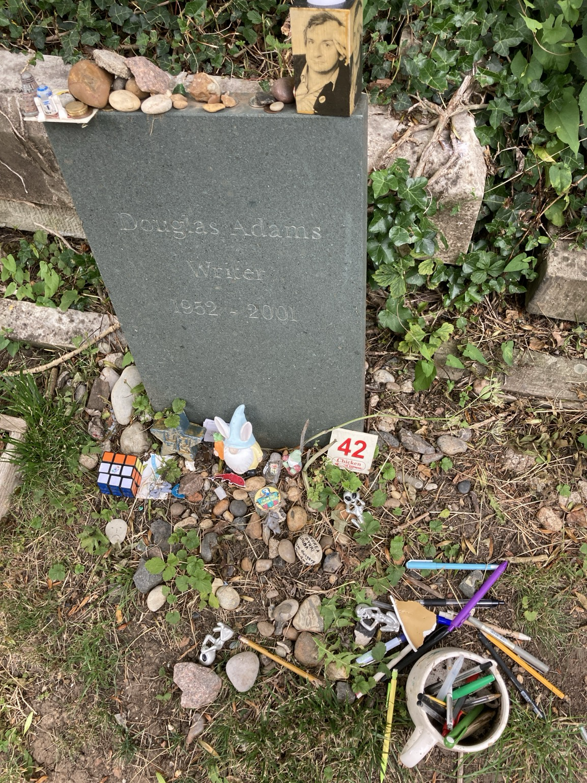 Headstone with, among other things, lots of writing implements, a Rubik cube, a space alien action gigure, …