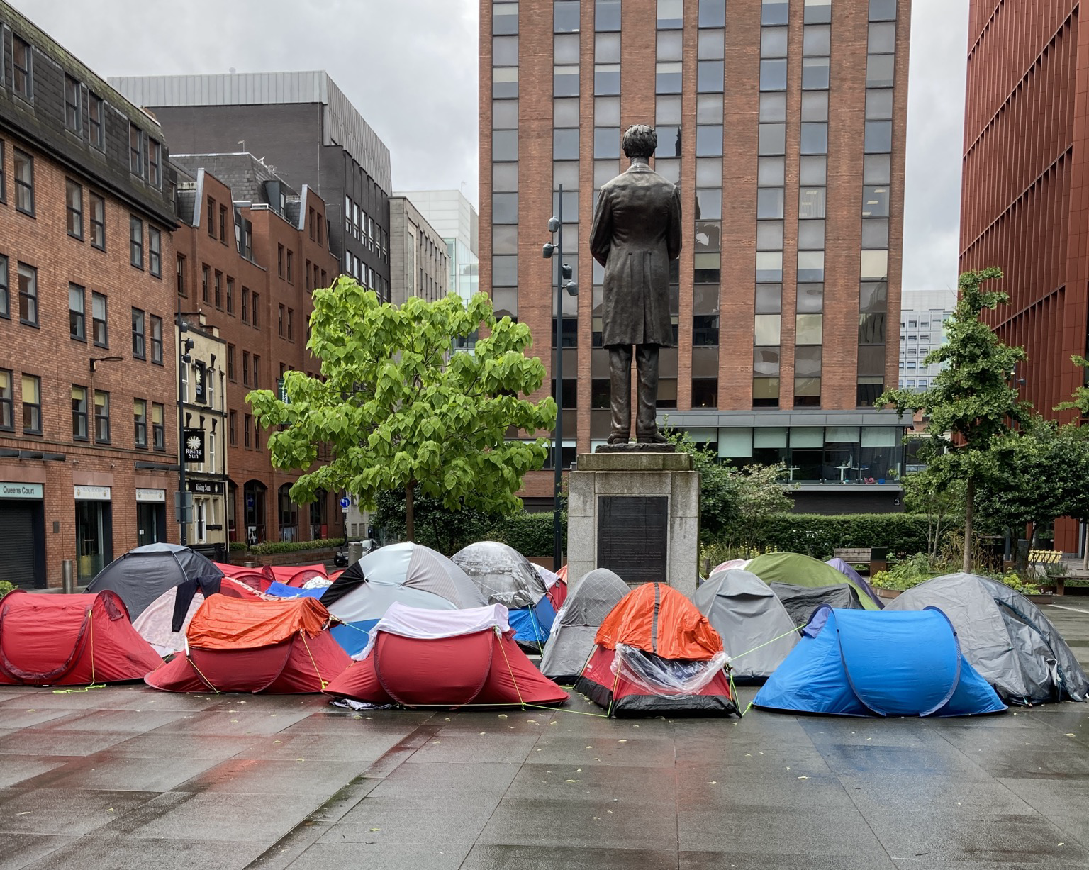 Dozens of nylon tents on a wet plaza at the back of a bronze statue of Lincoln standing