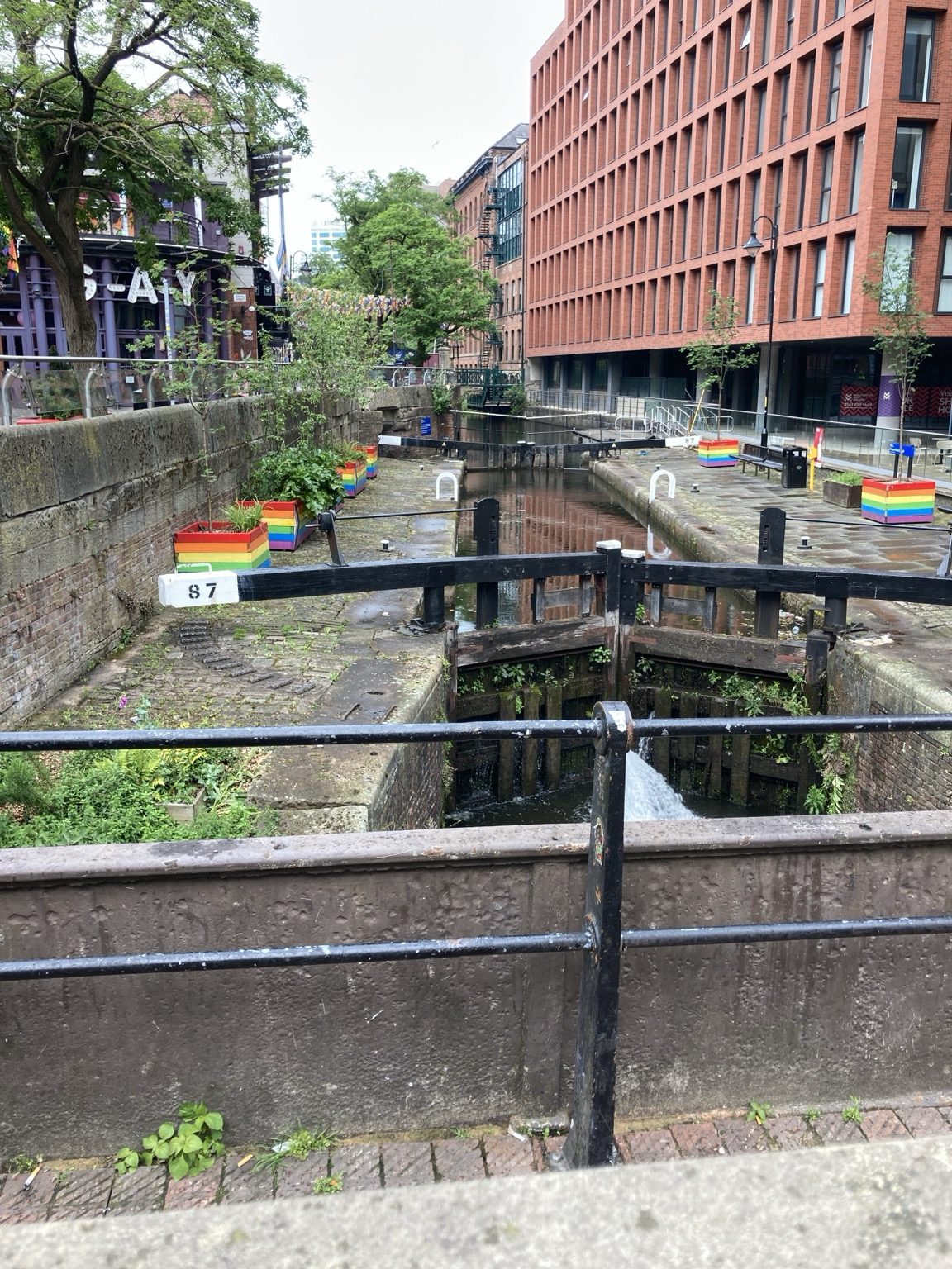 Looking down from a bridge to a narrow waterway with concrete banks with rainbow-painted boxes on either side