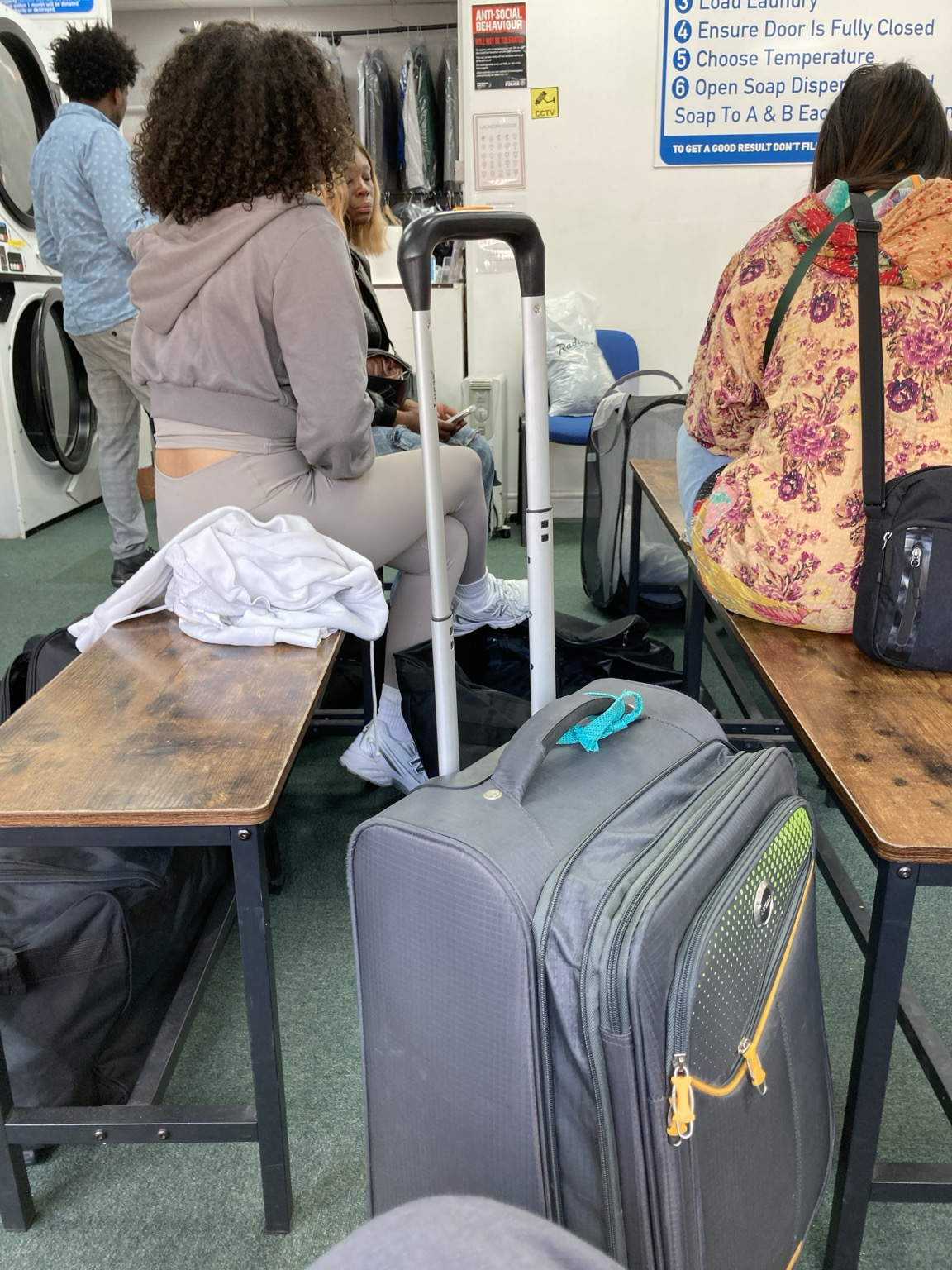 People waiting on wooden benches for machines to finish with their clothes