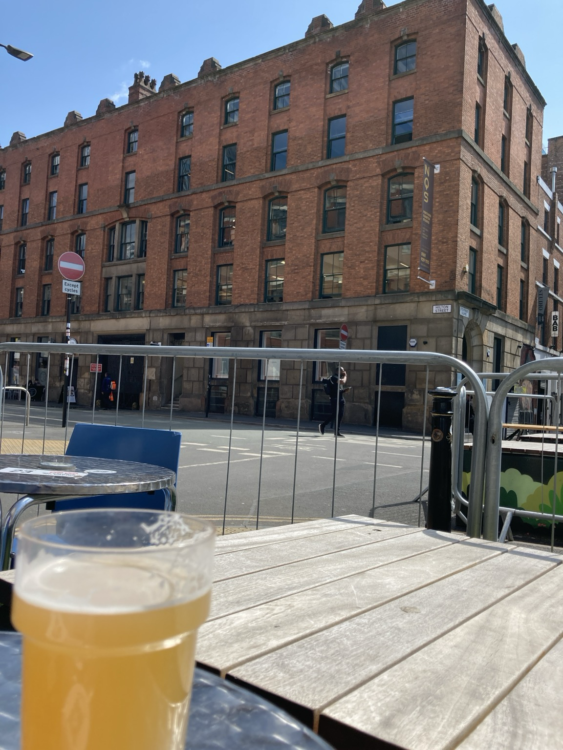 Foreground: pint of ale on metal table. Background: red brick Victorian building against blue sky