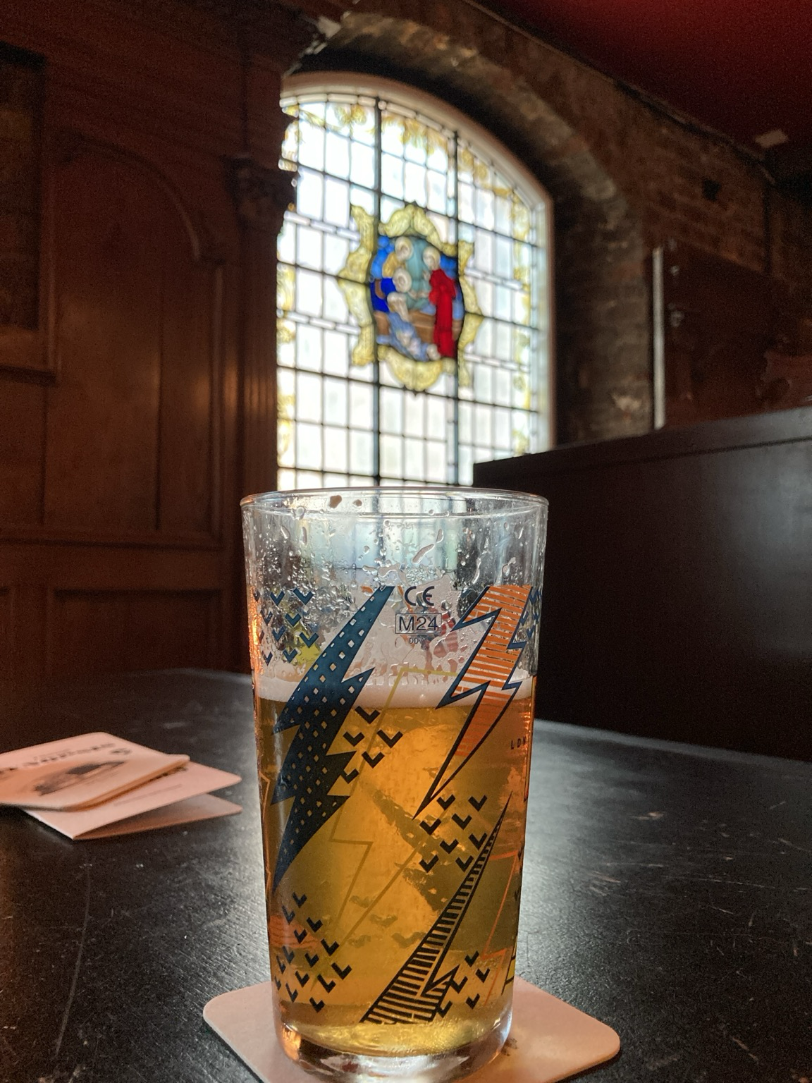 Looking through a pint glass and out a stained glass window from a dim booth