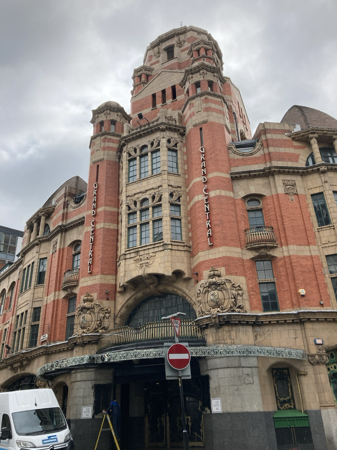 Ornate brick and sandstone exterior of a building with arched multistory windows, cupola and lots of other fancy details.