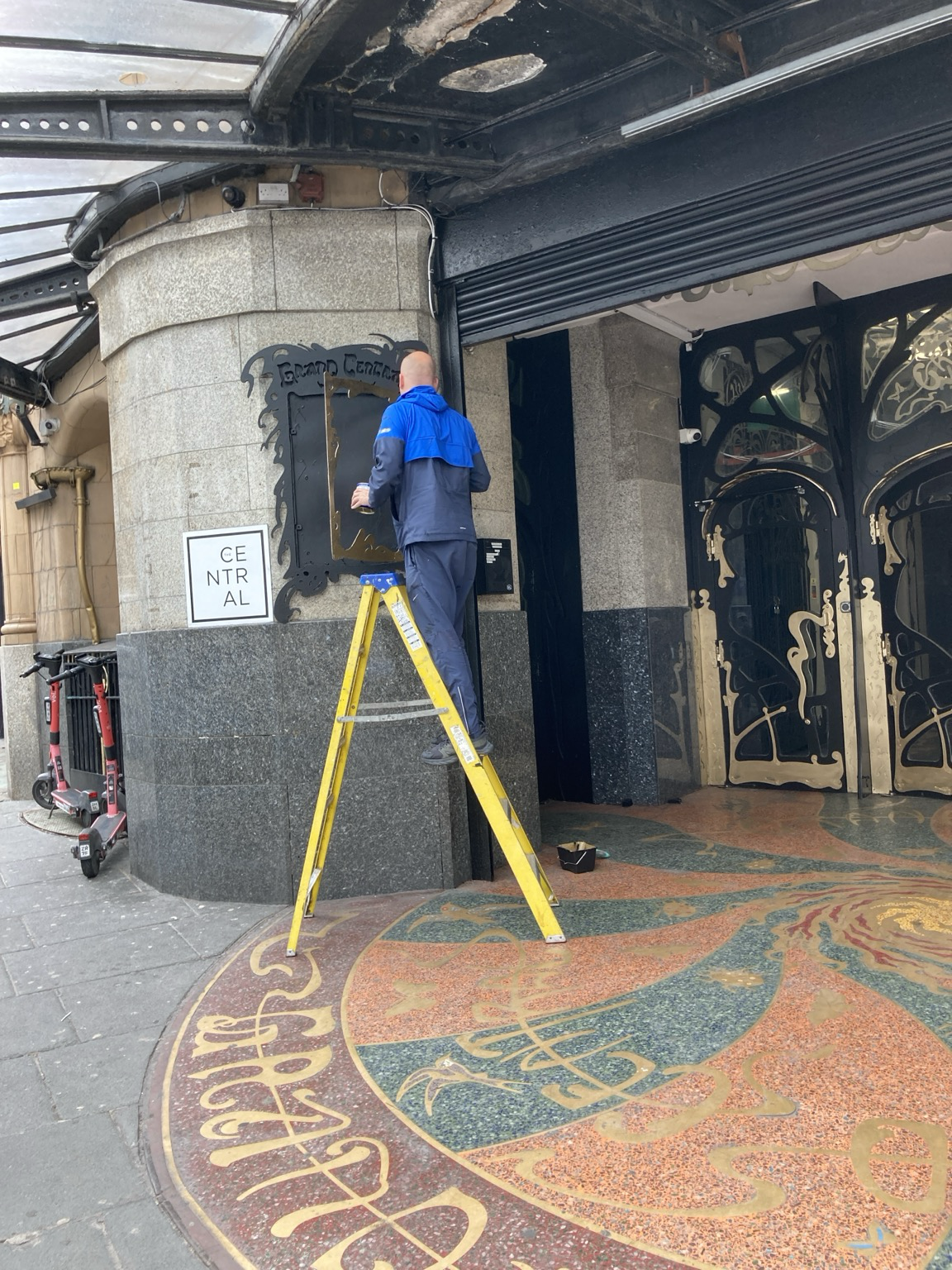 Man standing on high stepladder cleaning a window next to the locked entrance