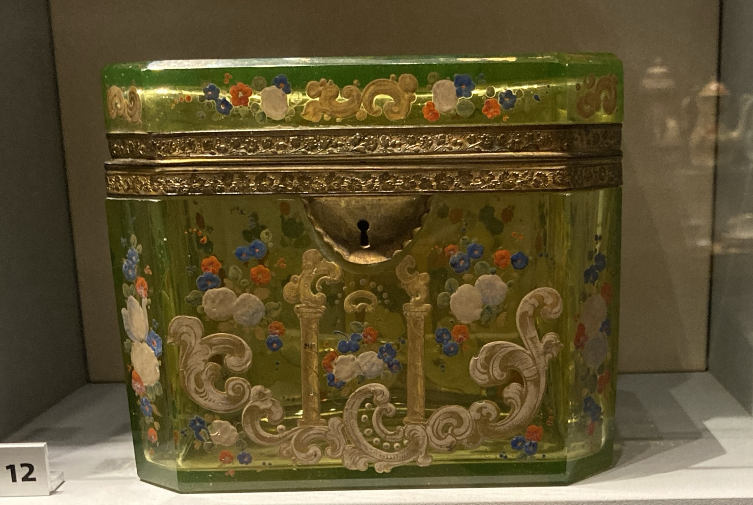 Caption: Tea caddy, glass, enamel and gilded metal, Bohemia, 1830-1850. Uranium gives this glass a bright green colour, the enamels and gold were painted on and then fired in a kiln.