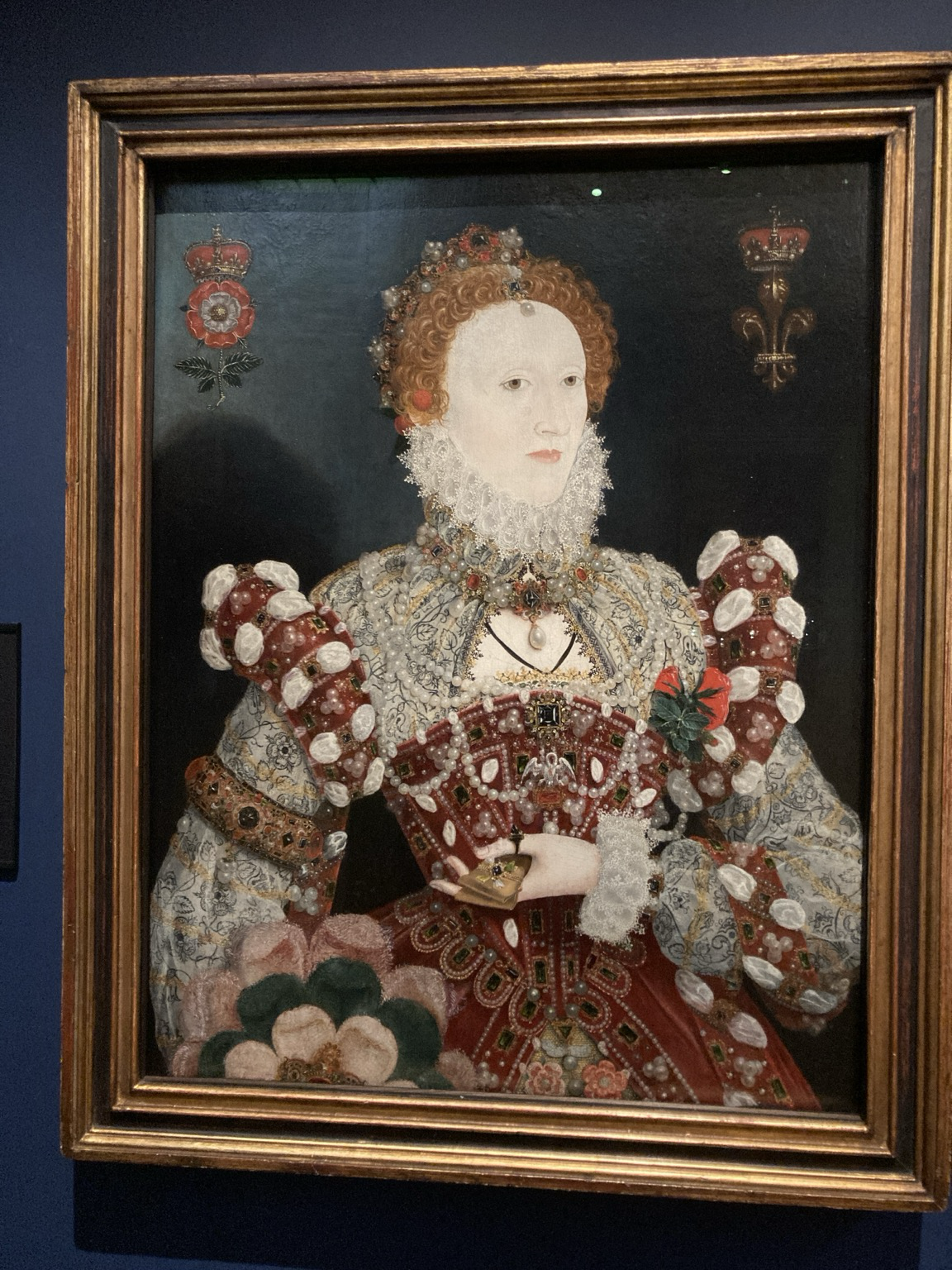 The pale face of the queen looks toward the viewer’s right ear, maybe. A ruff reaches her chin and ears. Her torso is encased in layers of lace, jewels and pearls.