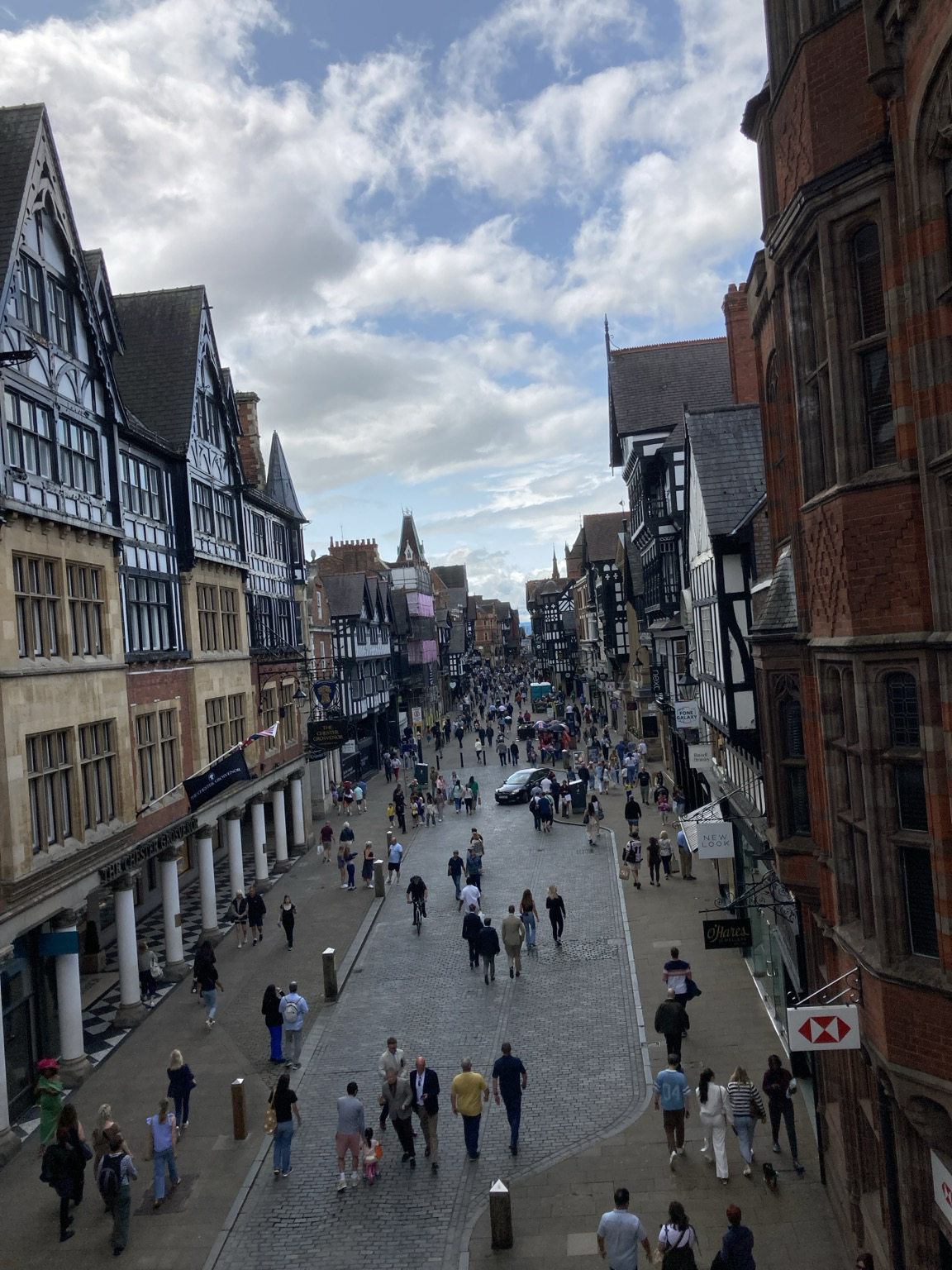 Seen from above, a street filled with pedestrians and lined with Tudor-ush buildings