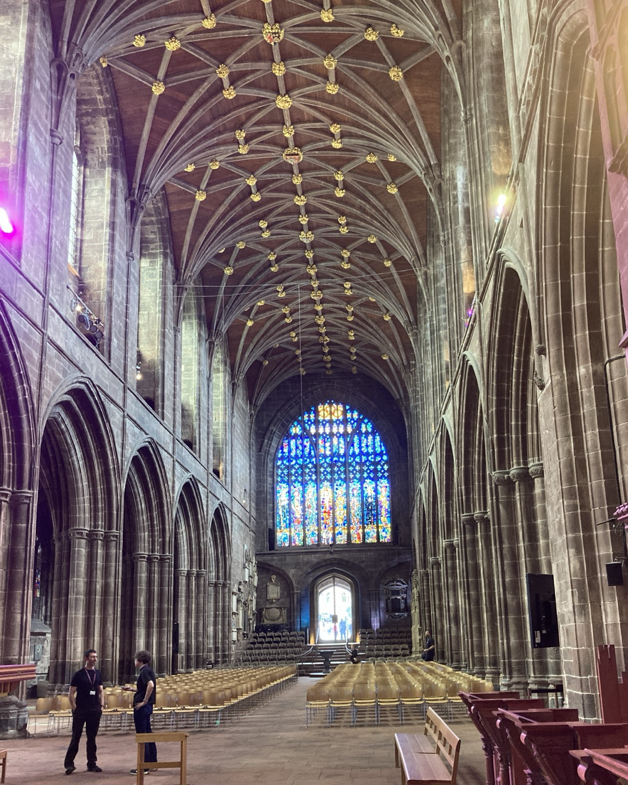 Looking down the nave toward a massive stained glass window, on either side arches leading to side aisles