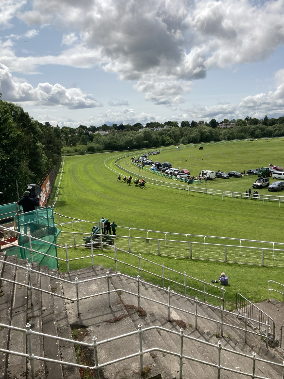 Horses ridden by jockeys in a tight group rounding a bend on a bright green grass track