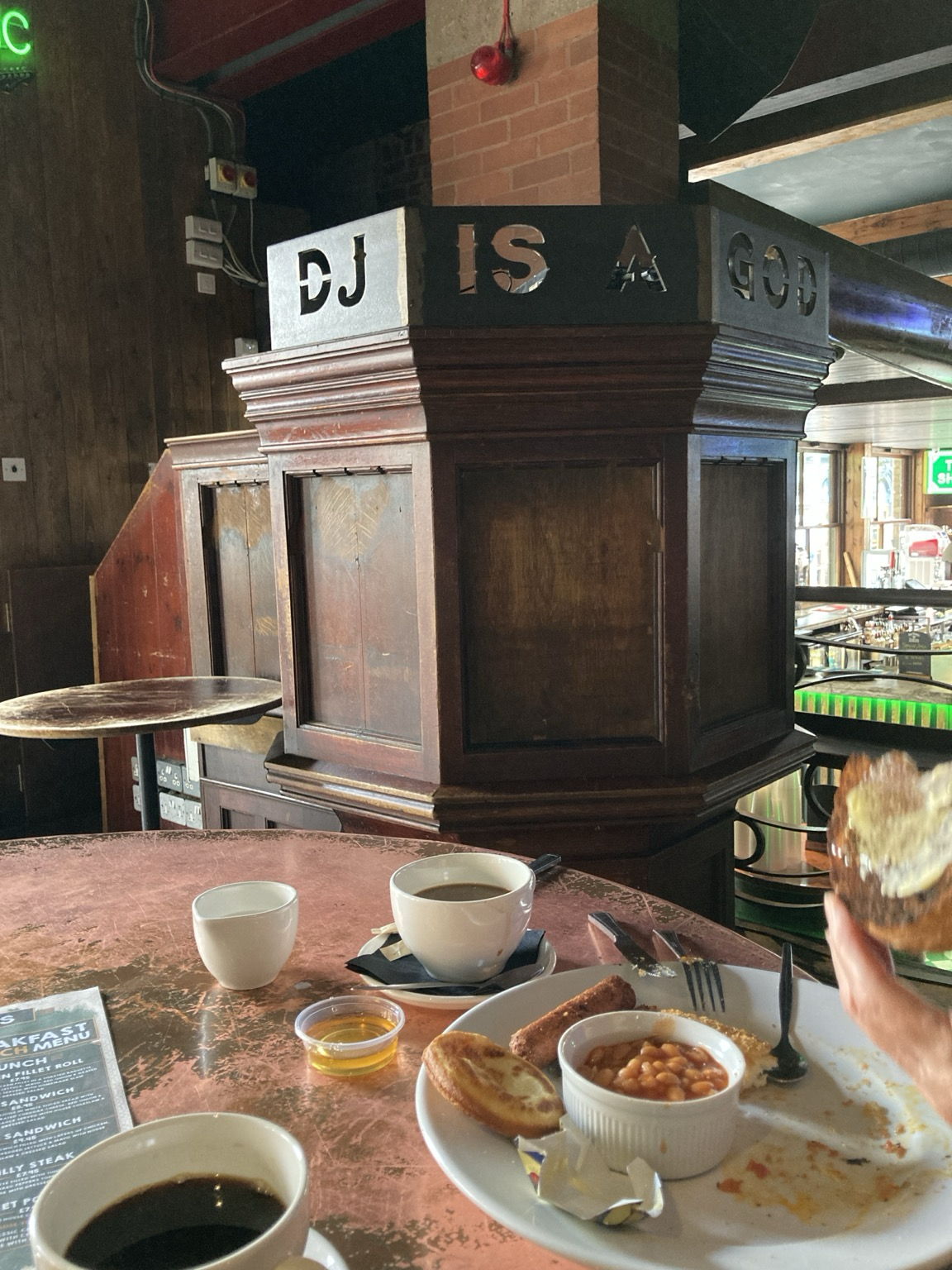 Breakfast dishes on a table under a DJ booth repurposed from a church altar with carved “DJ is a god”