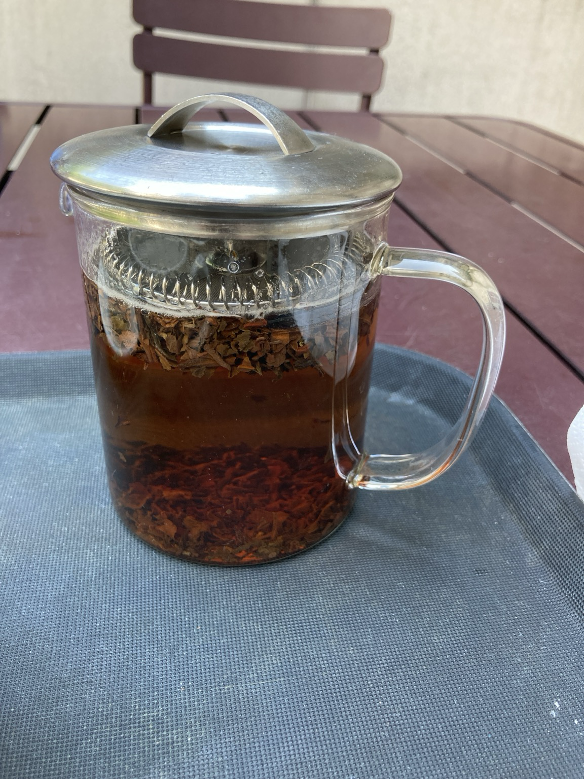 On a tray on a picnic style table, a beaker full of tea leaves swimming