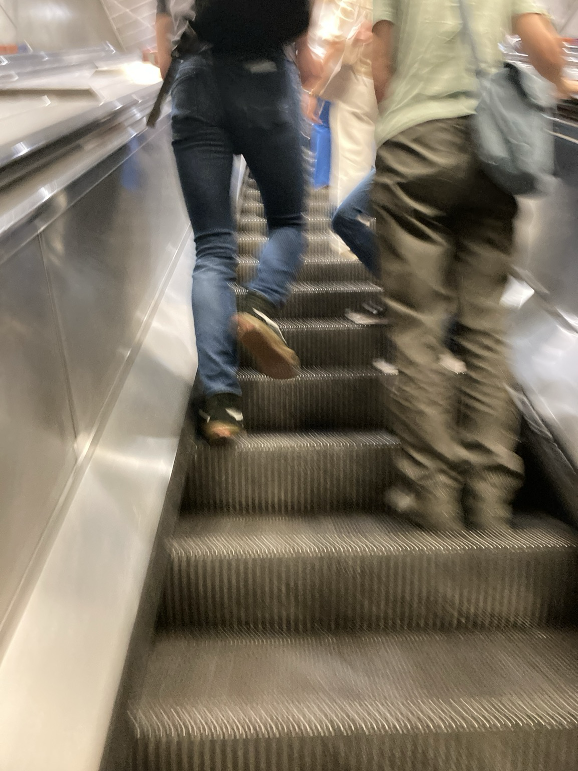 Looking upward on an escalator: one person on the left passes someone on the right
