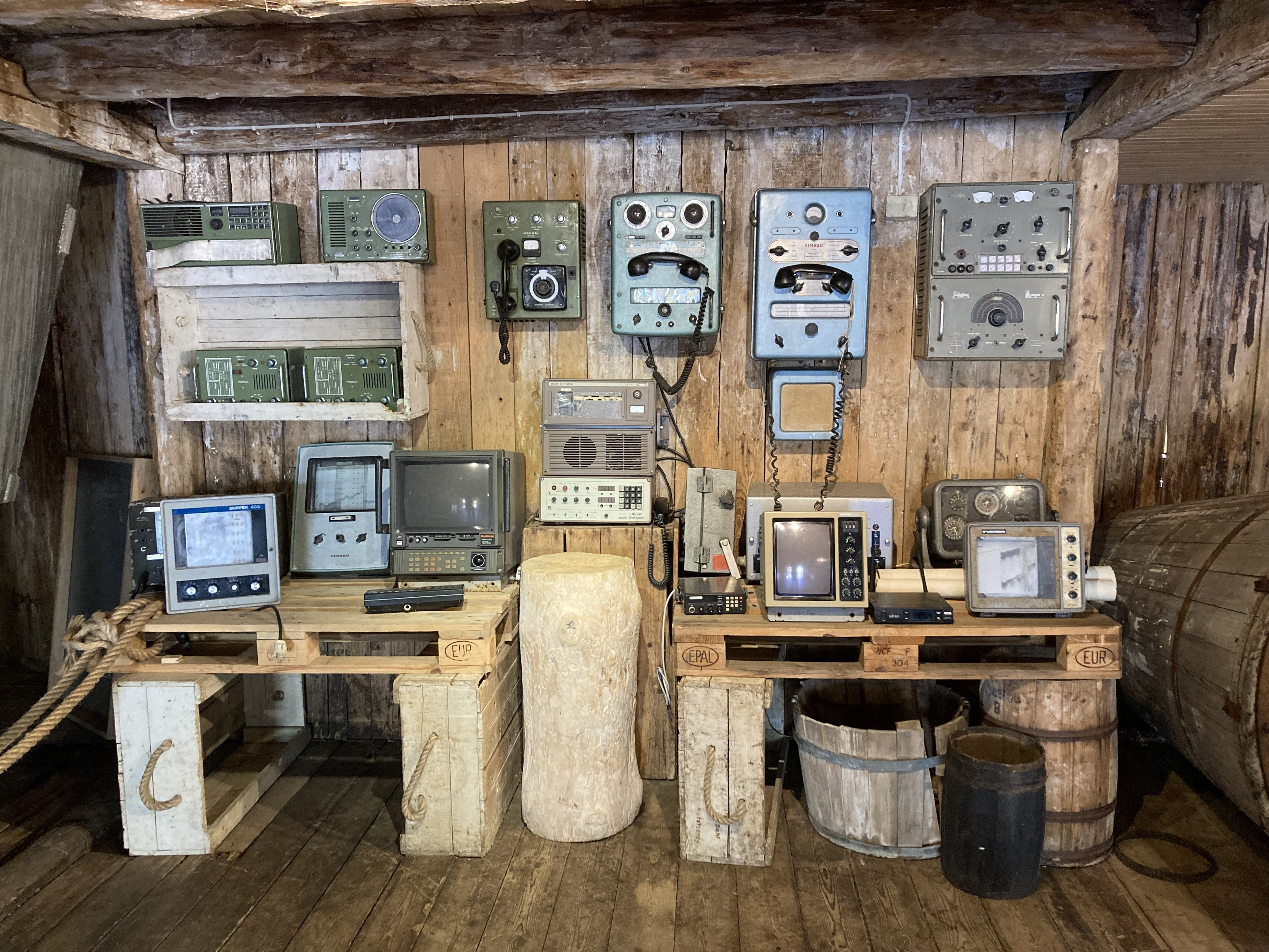 Zu sehen ist ein Raum komplett aus Holz. An einer Wand sind jede Menge alte Geräte (Funkgeräte, Telefone, etc.) montiert bzw. stehen auf Tischen. Zu sehen ist ein Raum komplett aus Holz. An einer Wand sind jede Menge alte Geräte (Funkgeräte, Telefone, etc.) montiert bzw. stehen auf Tischen.
