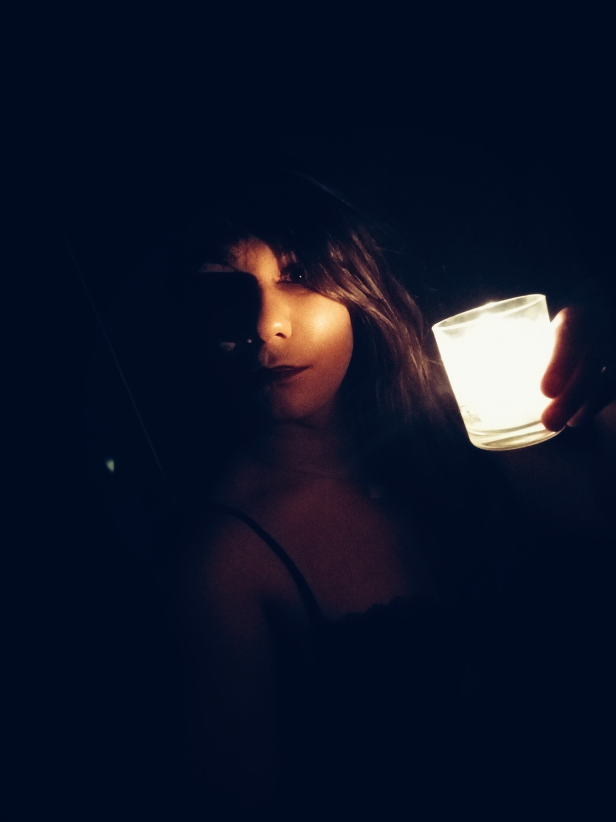 A dramatically lit portrait in chiaroscuro of a brunette holding a candle. Only part of her left cheek is visible. A dramatically lit portrait in chiaroscuro of a brunette holding a candle. Only part of her left cheek is visible.