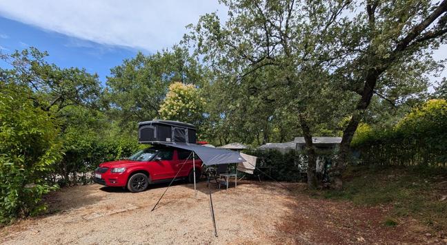 Ein Auto mit einem Dachzelt und einem am Auto befestigten tarp auf einer gesplitteten Campingplatzparzelle.