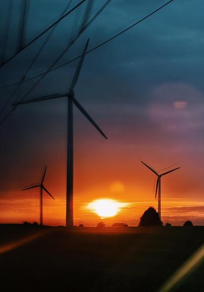 Sunset shot through the window of a driving train, right into the sun, a green turned black field in the front, some wind power around 