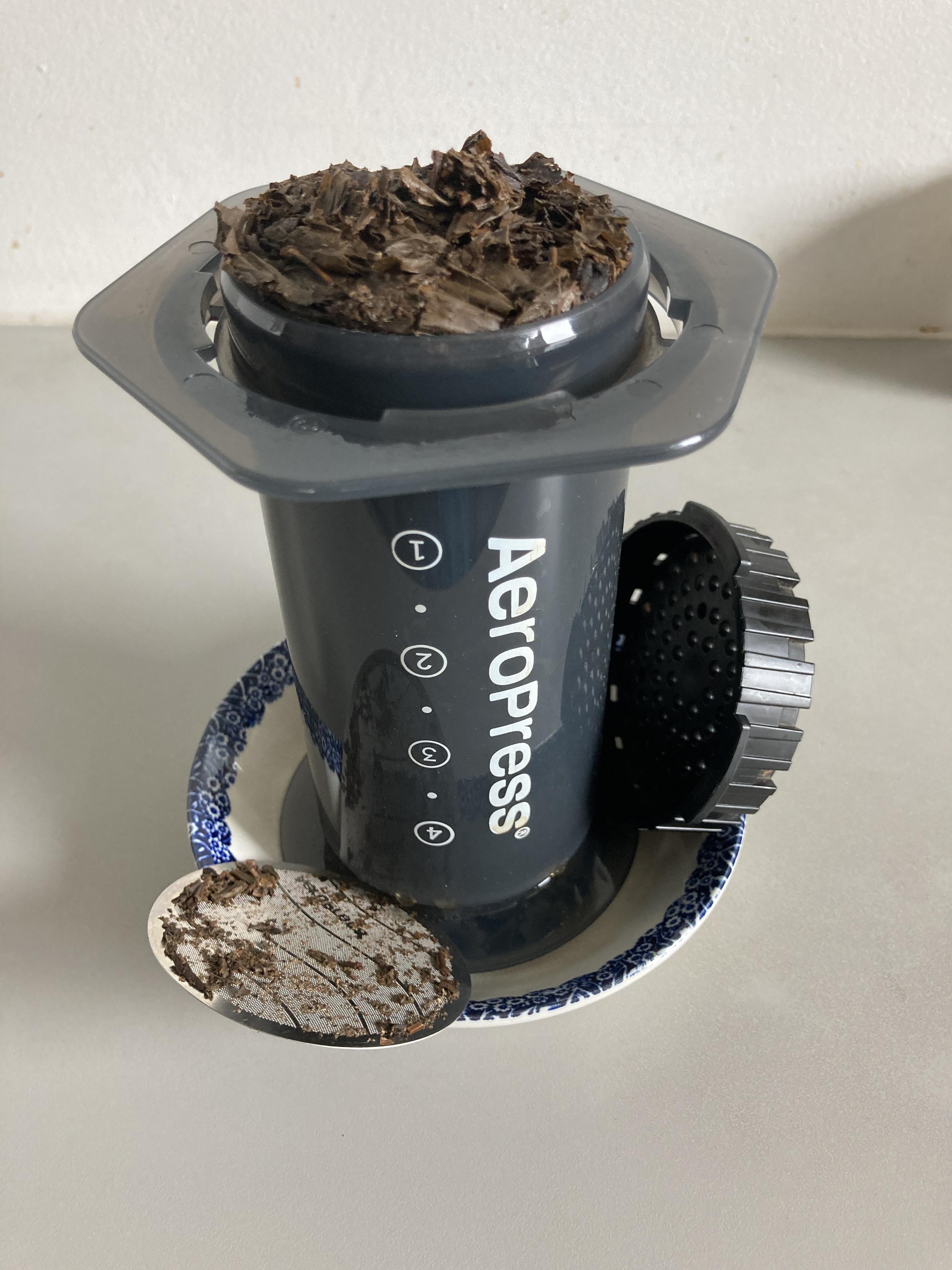 With its cap and filter off, the inverted Aeropress sits in a small dish with brewed leaves swelling out of the bottom of the piston.