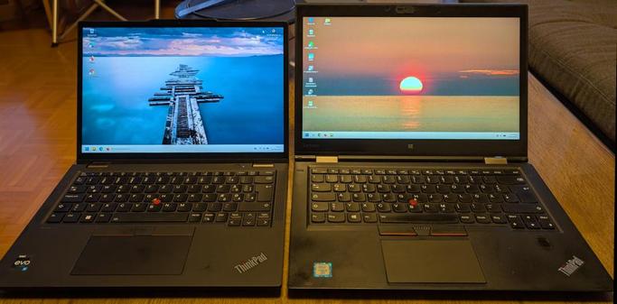 Zwei Laptops stehen auf einem Wohnzimmertisch nebeneinander. Beide Geräte sind schwarz und zeigen unterschiedliche Desktops. Das linke Gerät ist kleiner und hat auch ein kleineres Display.
