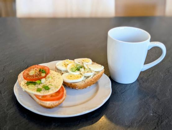 Auf einem Tisch steht eine Tasse Kaffe und ein Teller mit einem Tomate-Mozarella- und einem Eibrötchen.